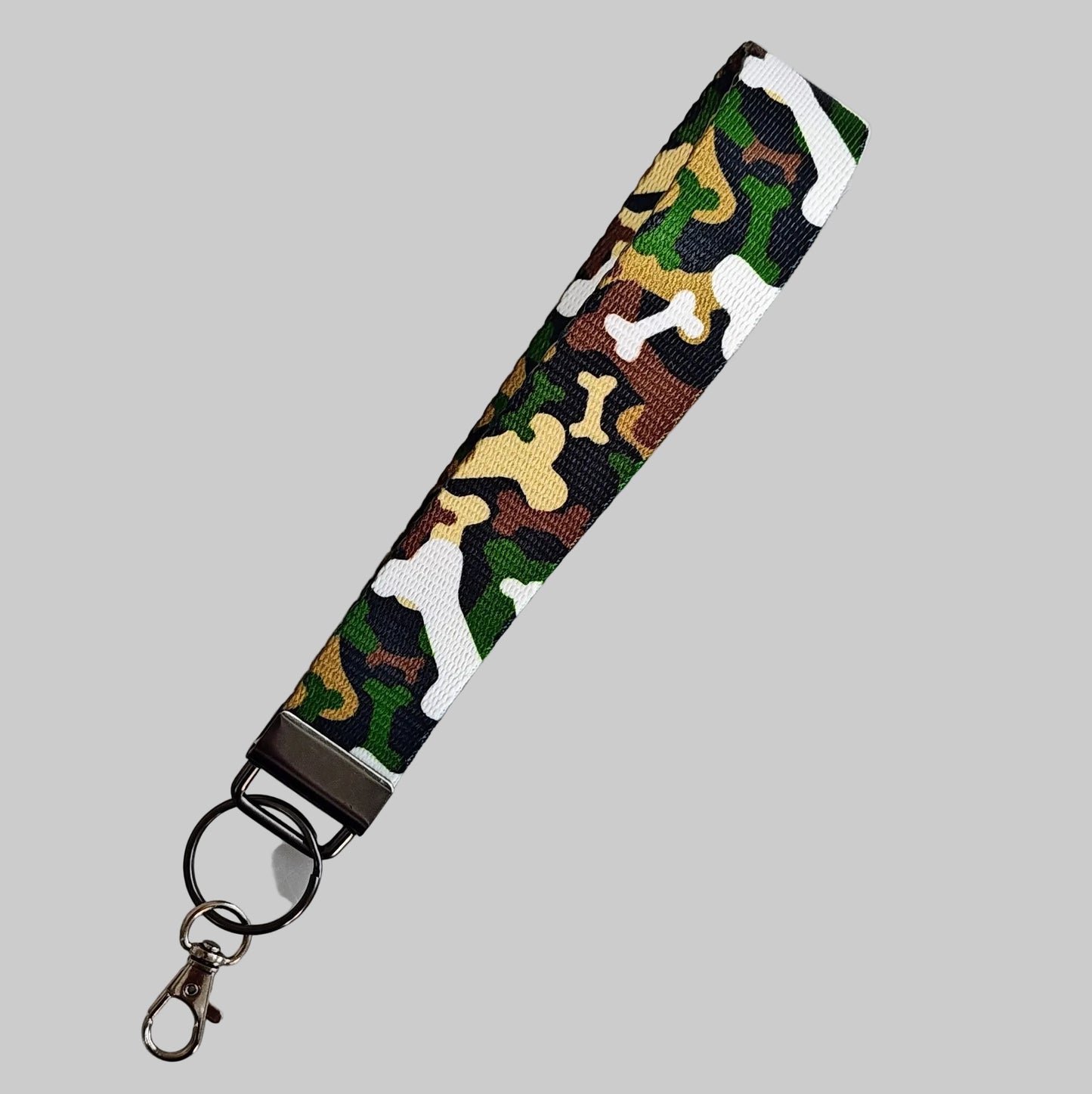 A fabric wristlet keychain strap featuring a woodland camouflage pattern in green, brown, beige, and white, finished with a black metal clasp and split ring, shown on a light gray background.
