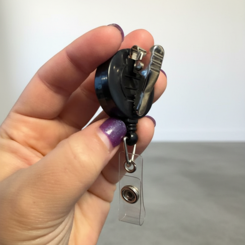Hand holding a small black and silver reel with a clear badge holder on a neutral background