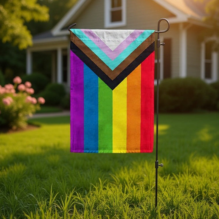 Colorful garden flag with a Progress Pride flag design on a grassy lawn in front of a house.