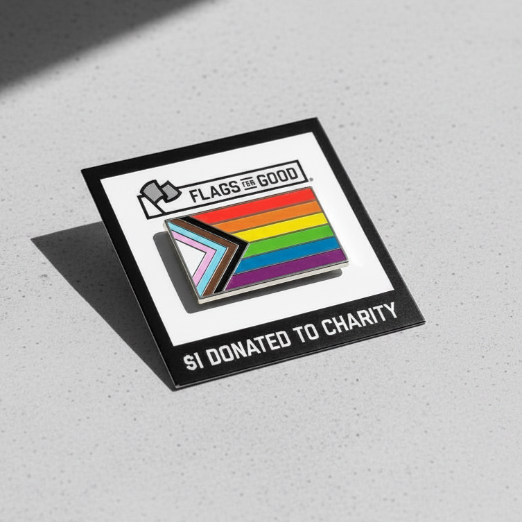 Pin with Progress Pride flag design on a gray concrete surface