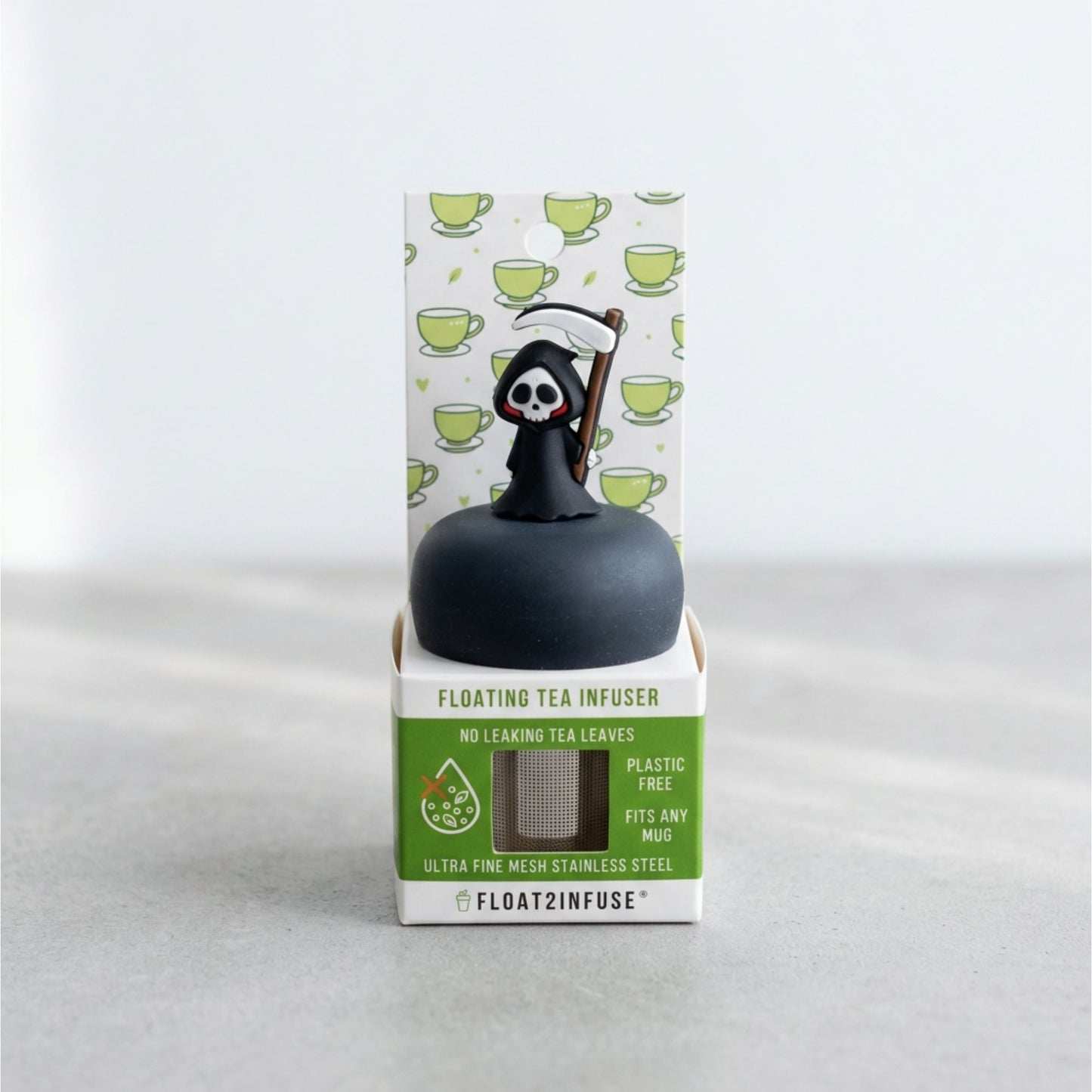 A floating tea infuser by Float2Infuse in its retail packaging, featuring a black spherical infuser topped with a grim reaper figure holding a scythe, set against a light gray background.