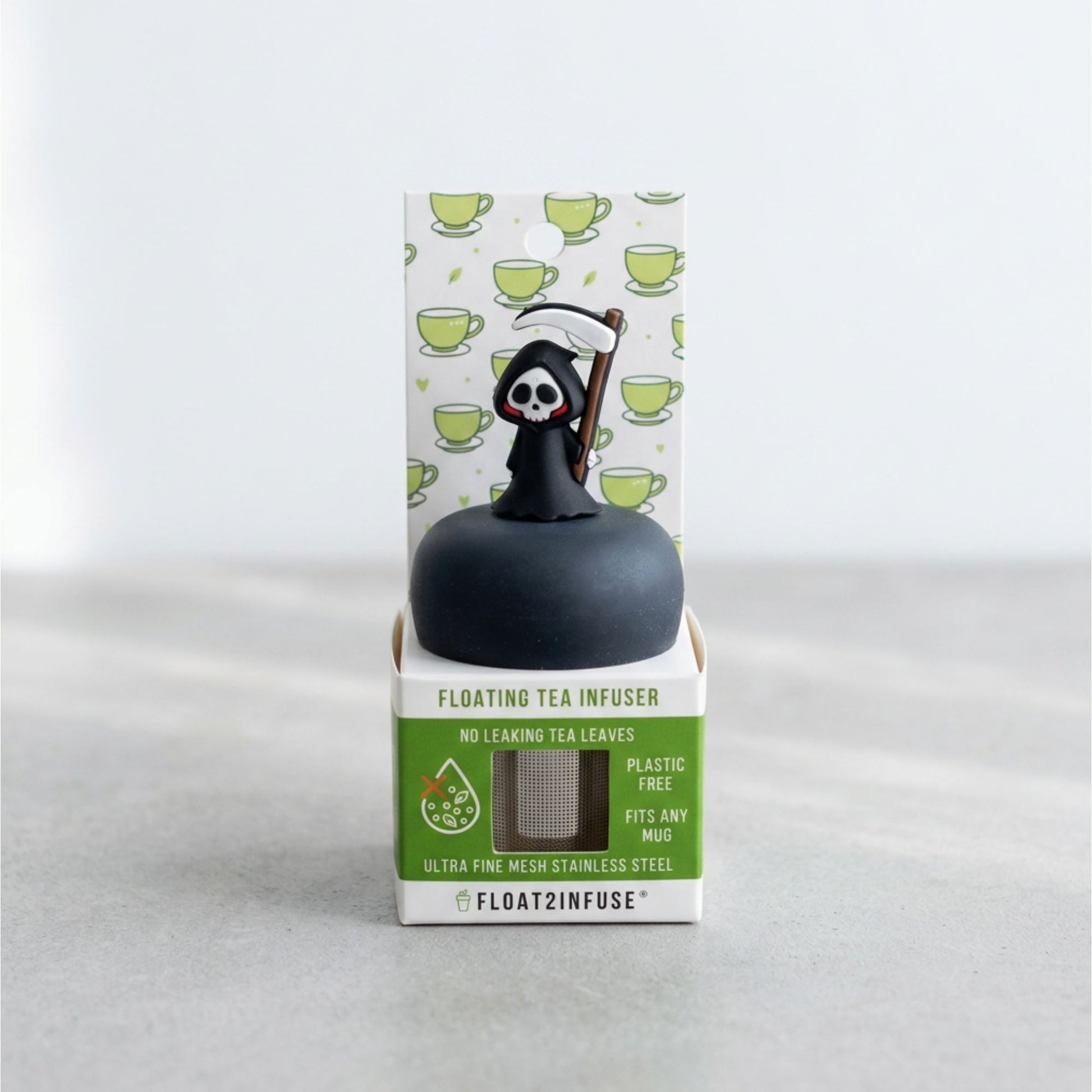 A floating tea infuser by Float2Infuse in its retail packaging, featuring a black spherical infuser topped with a grim reaper figure holding a scythe, set against a light gray background.